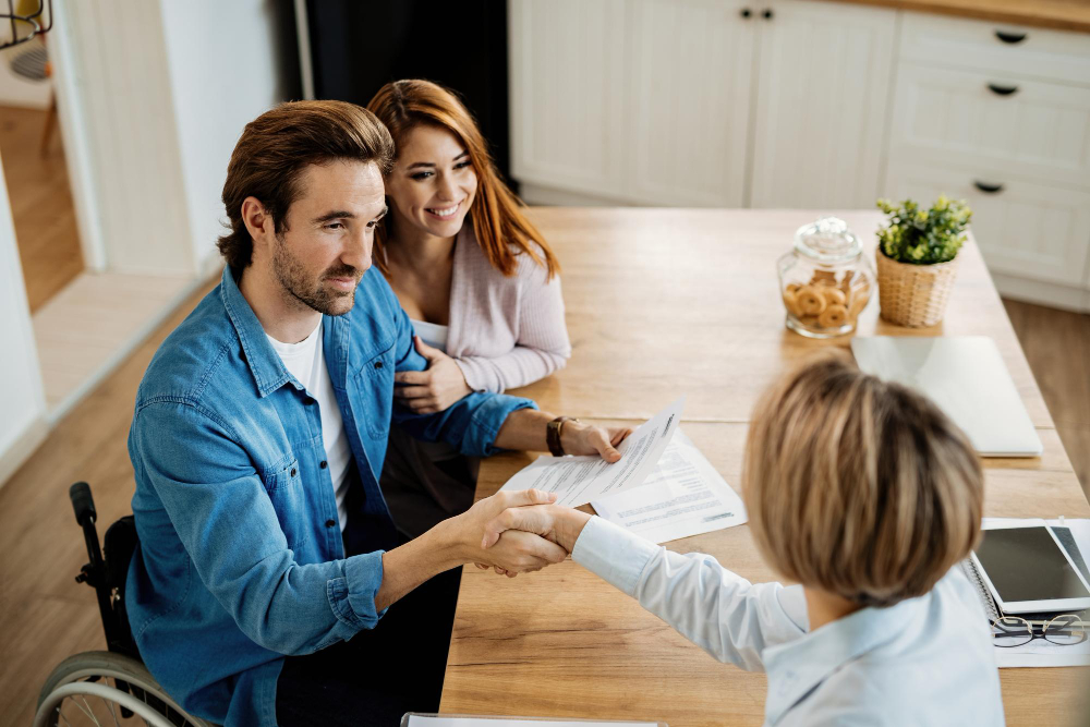 young happy couple making agreement with their insurance agent meeting home focus is man wheelchair